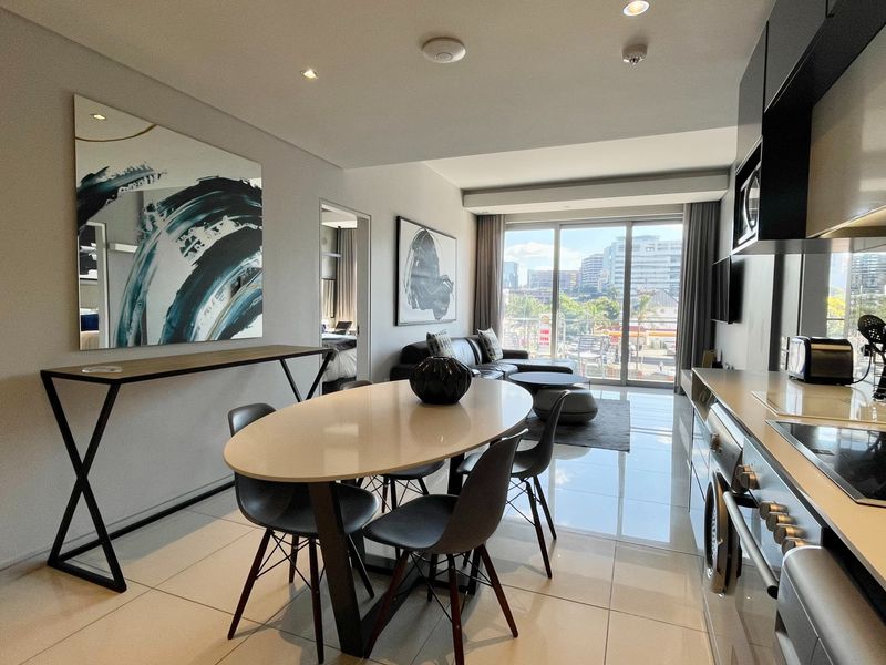 Modern open-plan living area featuring a sleek kitchen with integrated appliances, polished floor tiles, and large sliding doors leading to a balcony with city views.