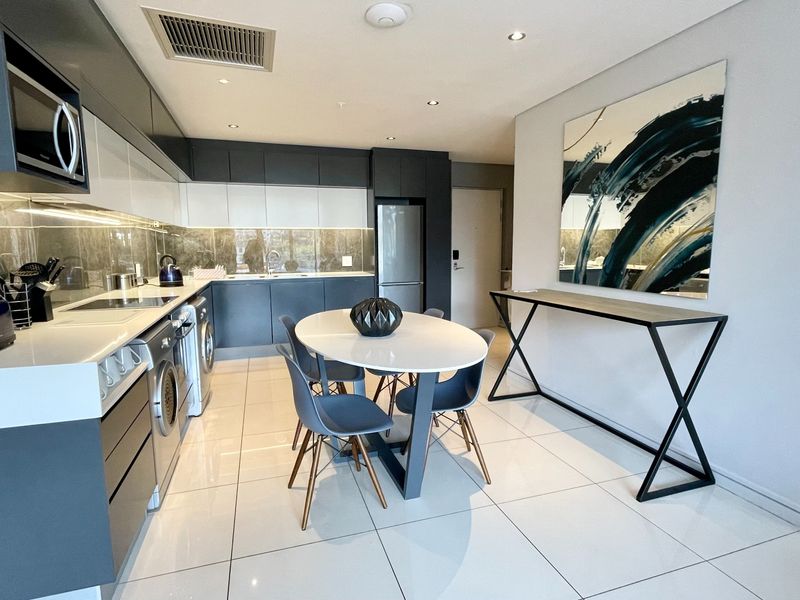 Modern open-plan kitchen featuring sleek two-tone cabinetry, stone countertops, integrated appliances, and polished tiled flooring, seamlessly flowing into the dining area.