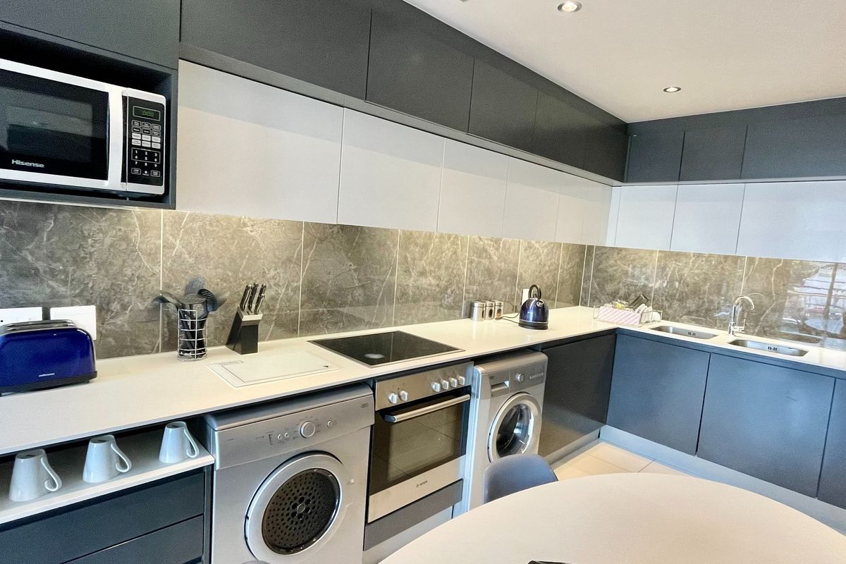 Modern kitchen featuring sleek two-tone cabinetry, stone-look backsplash, integrated oven, electric hob, built-in microwave, and double sink with recessed lighting.