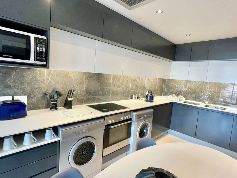 Modern kitchen featuring sleek two-tone cabinetry, stone-look backsplash, integrated oven, electric hob, built-in microwave, and double sink with recessed lighting.