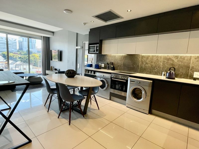 Modern open-plan apartment featuring a sleek kitchen with integrated appliances, stone splashback, and high-gloss cabinetry, flowing into a bright living area with balcony access.