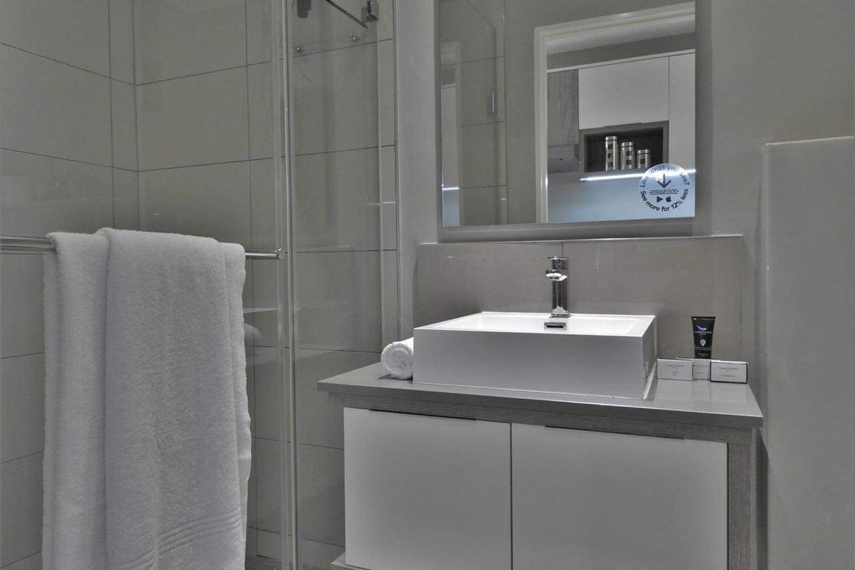 Modern bathroom featuring a sleek vanity with a vessel sink, wall-mounted mirror, and a glass-enclosed shower with neutral tiling.