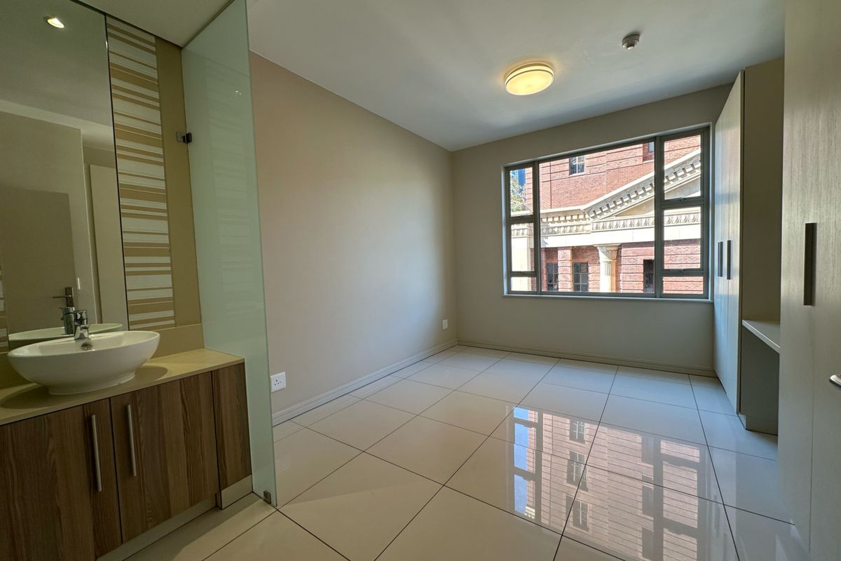 A bright bedroom featuring large tiled flooring, built-in cabinetry, and an integrated vanity area with a modern basin.