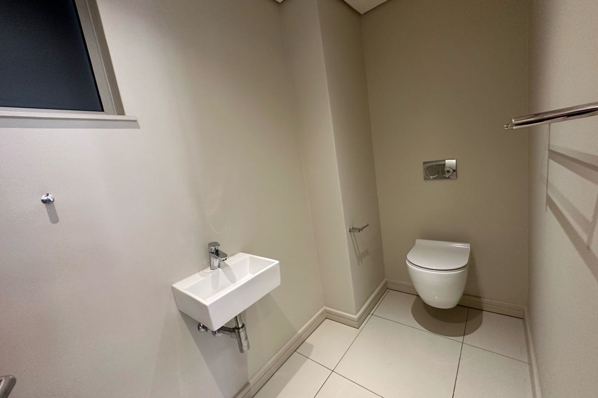 A modern guest cloakroom featuring a wall-mounted toilet with a concealed cistern, a compact wall-hung basin, and neutral tiled flooring.