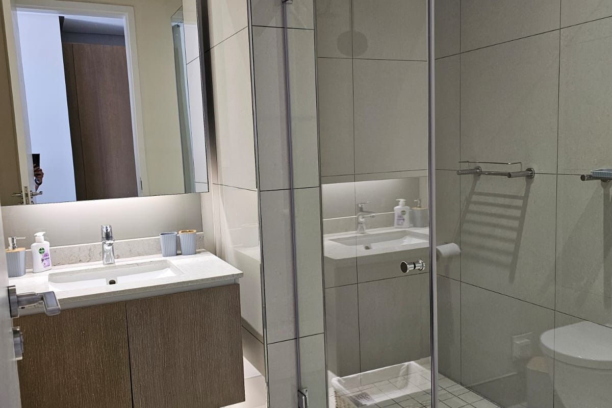 Modern bathroom featuring a floating vanity with stone countertop, large wall mirror, and a spacious walk-in shower with glass enclosure and tiled flooring.