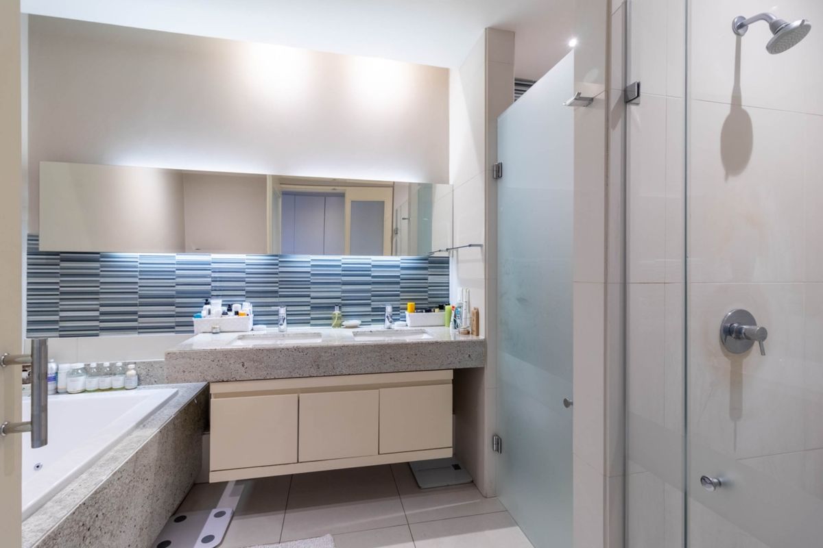 Modern bathroom featuring a double vanity with stone countertop, integrated sinks, a glass-enclosed shower, and a bathtub with tiled surround.