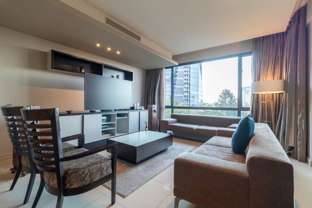 A modern living room featuring large windows with city views, recessed ceiling lighting, and built-in cabinetry for media storage.