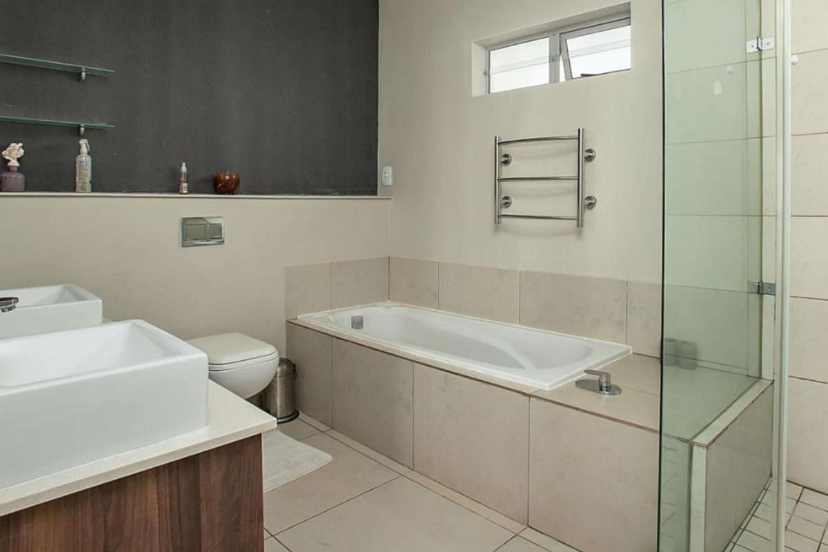 Modern bathroom featuring a double vanity, a built-in bathtub, a glass-enclosed shower, and a heated towel rail.