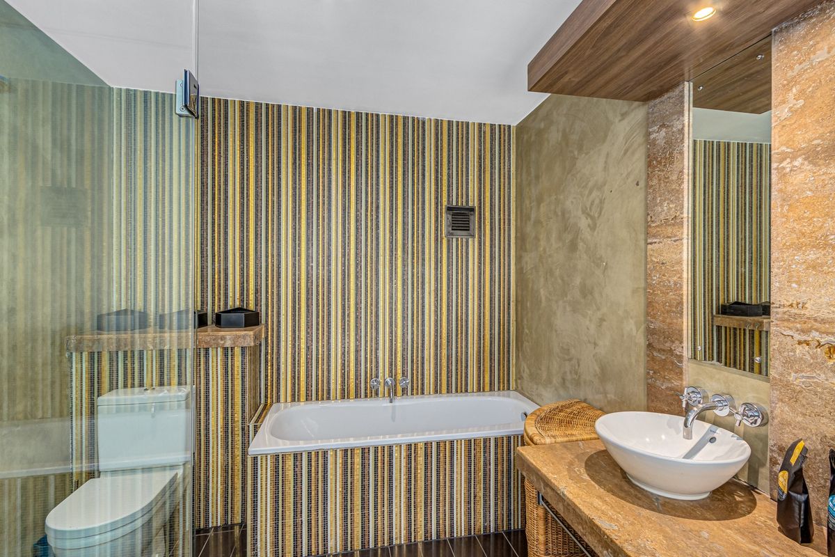 A modern bathroom featuring a built-in bathtub with mosaic tile surround, a stone vanity top with a vessel sink, and a glass-enclosed shower area.