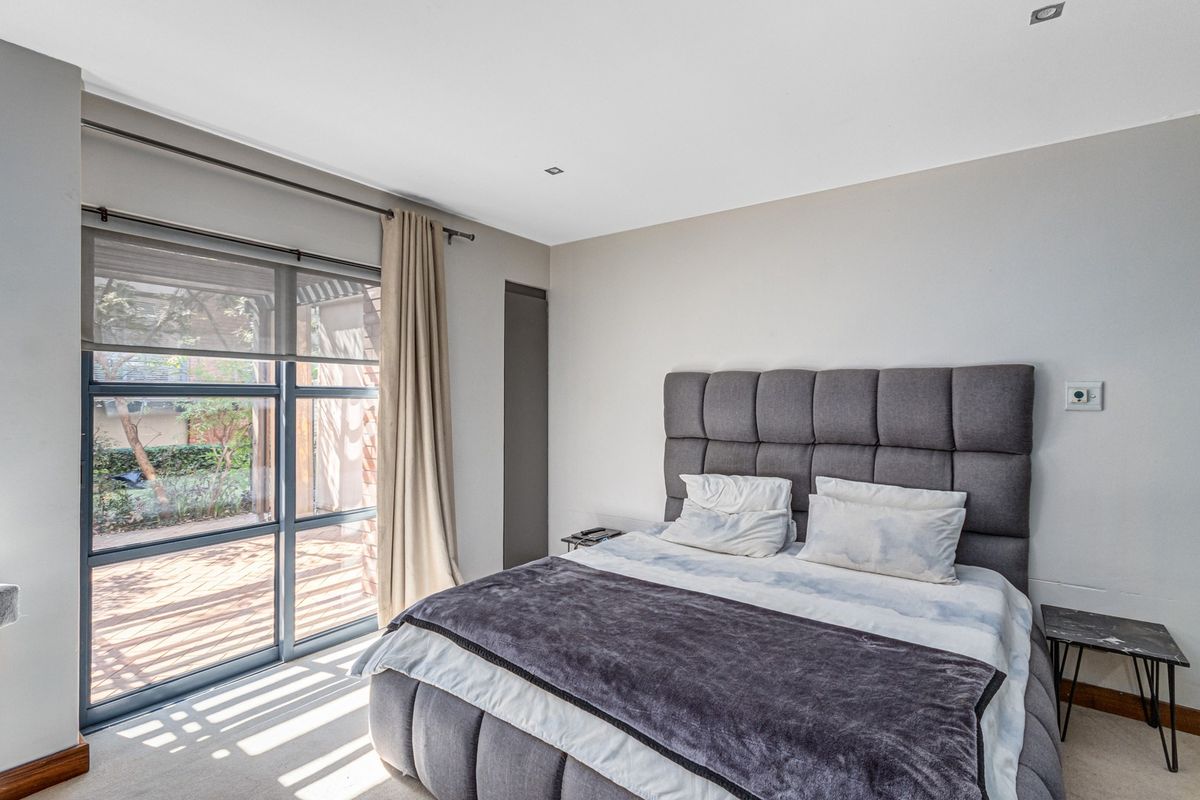 A bright bedroom featuring large floor-to-ceiling windows with direct access to an outdoor patio area, finished with neutral walls and recessed lighting.