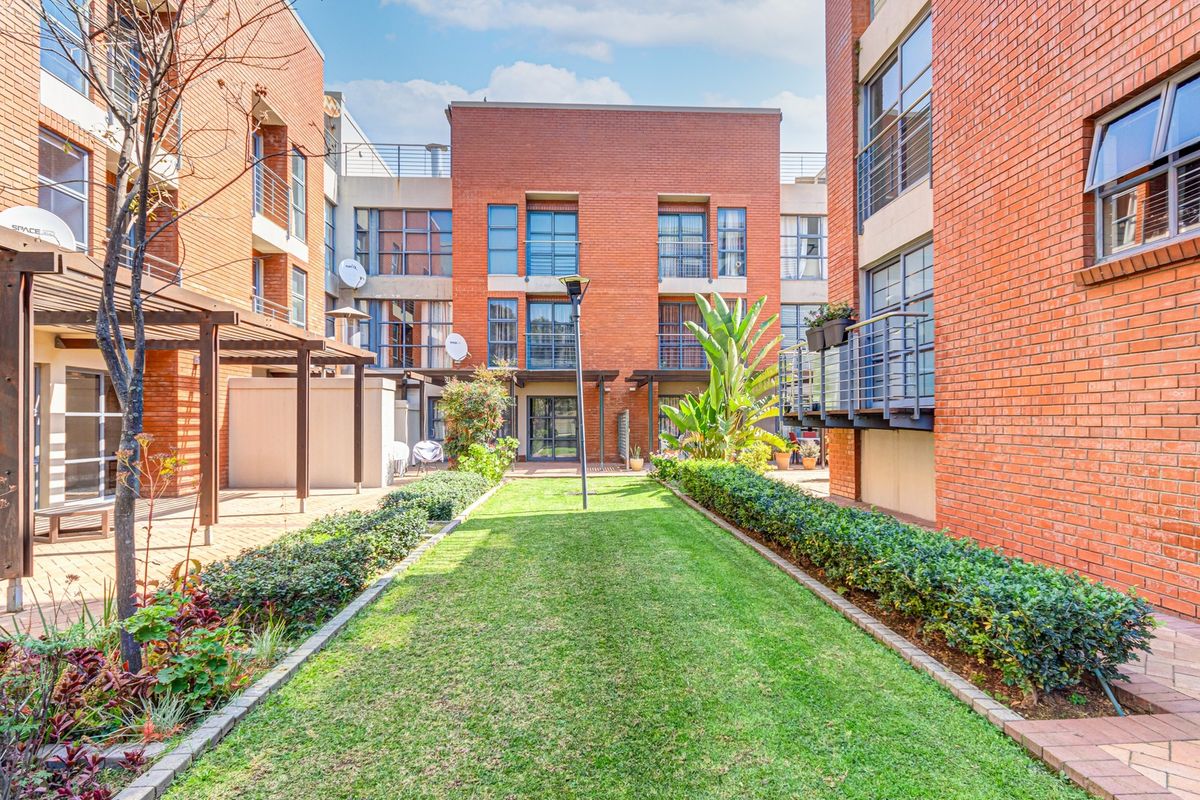 A well-maintained central courtyard area featuring a manicured lawn, landscaped garden beds, and paved walkways between brick apartment building blocks.