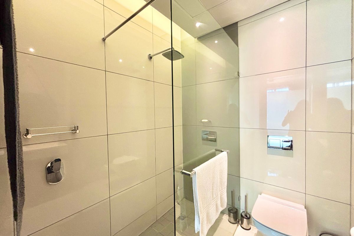 Modern bathroom featuring a glass-enclosed walk-in shower, wall-mounted toilet with concealed cistern, and large format neutral wall tiles.