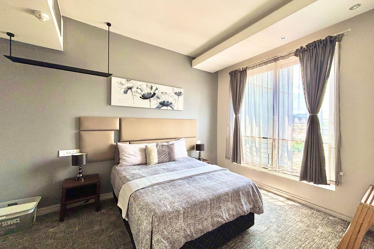A well-lit bedroom featuring a modern upholstered headboard, recessed ceiling detail, and large windows providing natural light.