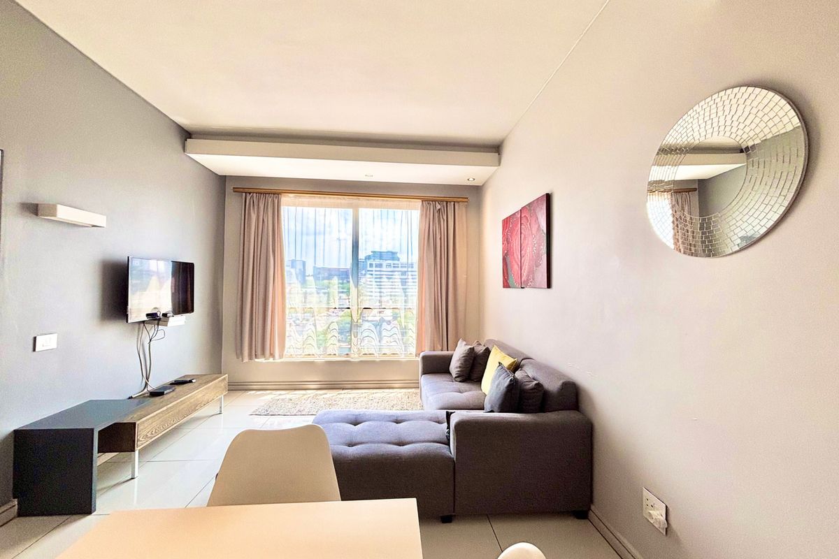 A bright and modern living room featuring large windows with natural light, tiled flooring, and a neutral color palette.