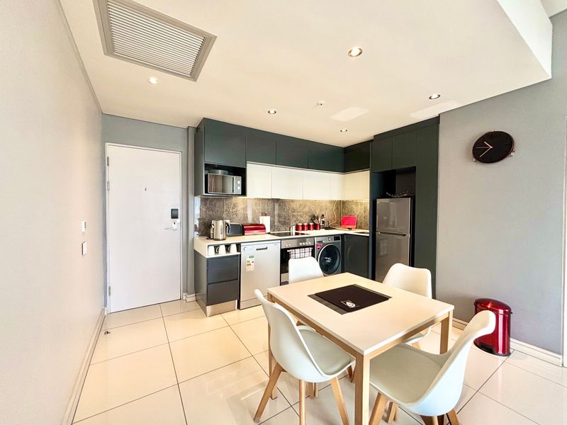 Modern open-plan kitchen and dining area featuring sleek two-tone cabinetry, integrated appliances, stone-look backsplash, and polished tiled flooring.