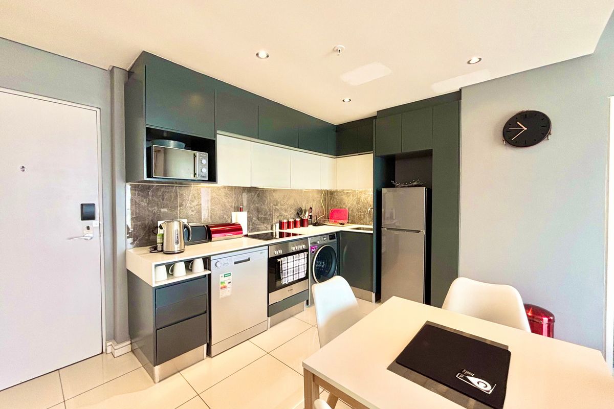 Modern kitchen featuring dark and light cabinetry, stone countertops, integrated appliances, tiled backsplash, and recessed lighting in an open-plan layout.