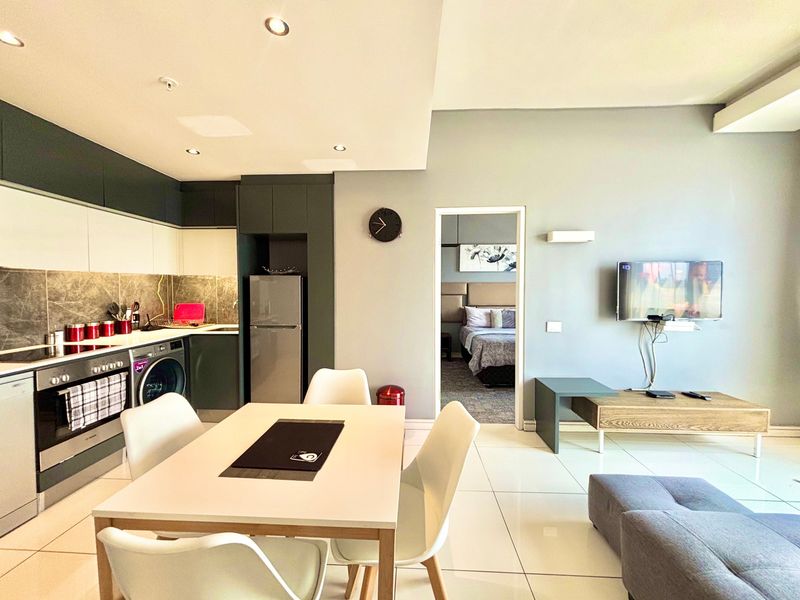 Modern open-plan living area featuring a sleek kitchen with integrated appliances, tiled flooring, and recessed lighting, seamlessly connecting to the adjacent bedroom.