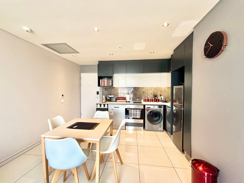 Modern open-plan kitchen featuring sleek cabinetry, stone backsplash, and integrated appliances, seamlessly flowing into the dining area with polished tiled flooring.