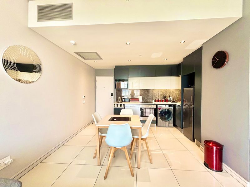 Modern open-plan kitchen and dining area featuring sleek built-in cabinetry, stone backsplash, integrated appliances, and polished tiled flooring with recessed lighting.