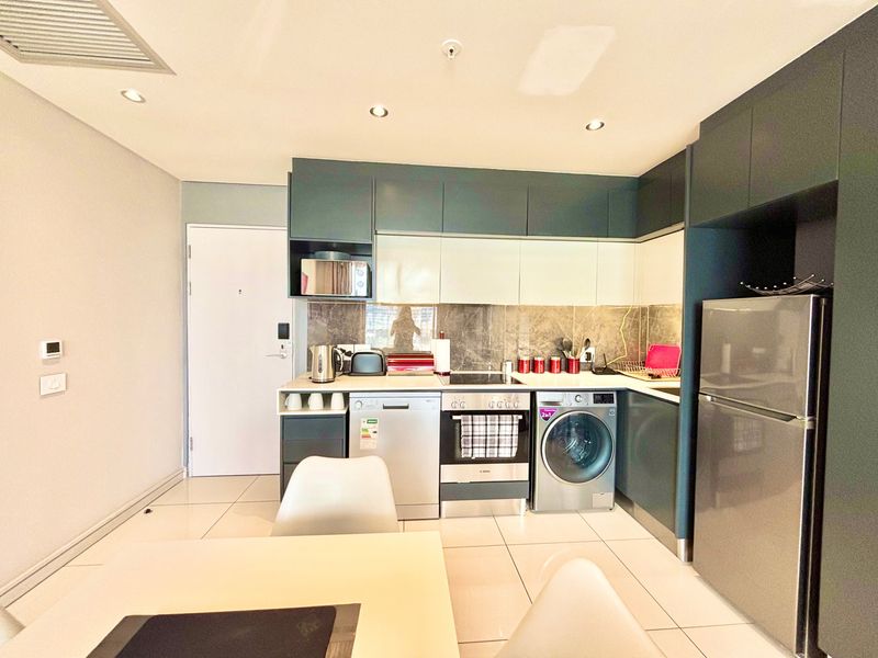 Modern kitchen featuring sleek dark and light cabinetry, stone backsplash, integrated appliances, and tiled flooring in an open-plan layout.