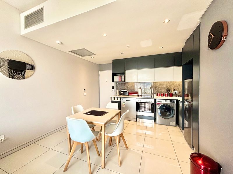 Modern open-plan kitchen and dining area featuring sleek built-in cabinetry, integrated appliances, stone splashback, and polished tiled flooring with recessed lighting.