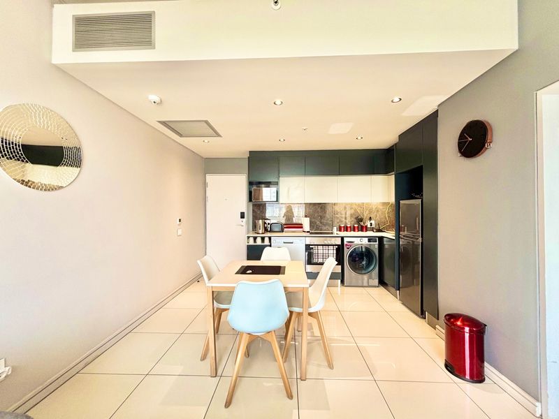 Modern open-plan kitchen and dining area featuring sleek built-in cabinetry, integrated appliances, tiled flooring, and recessed lighting in a well-maintained apartment setting.