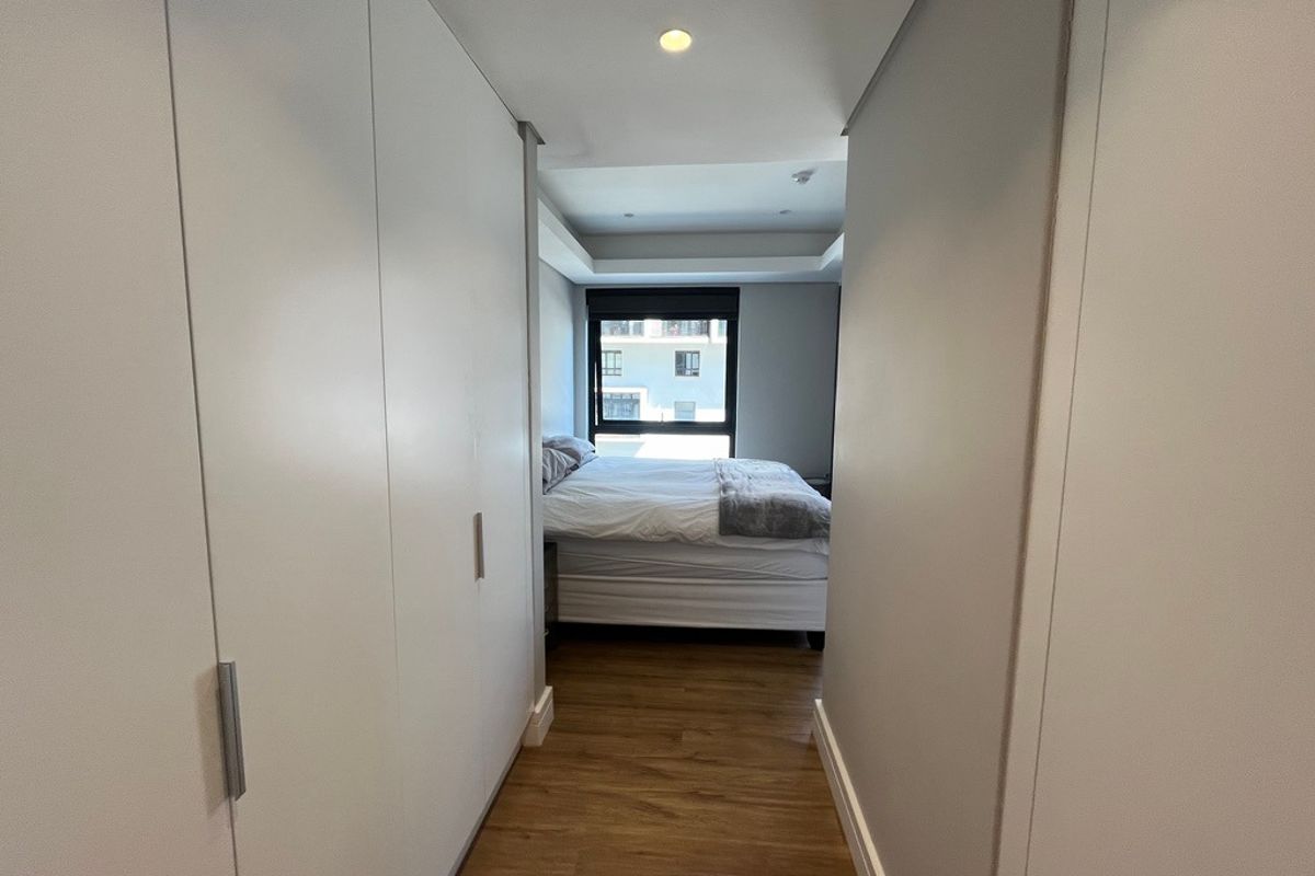 A well-maintained bedroom featuring built-in floor-to-ceiling cabinetry, recessed ceiling lighting, and wood-look flooring, leading to a bright sleeping area with a window.