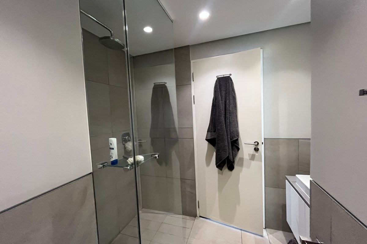Modern bathroom featuring a glass-enclosed walk-in shower with rainfall showerhead, neutral wall tiling, and a sleek vanity unit.