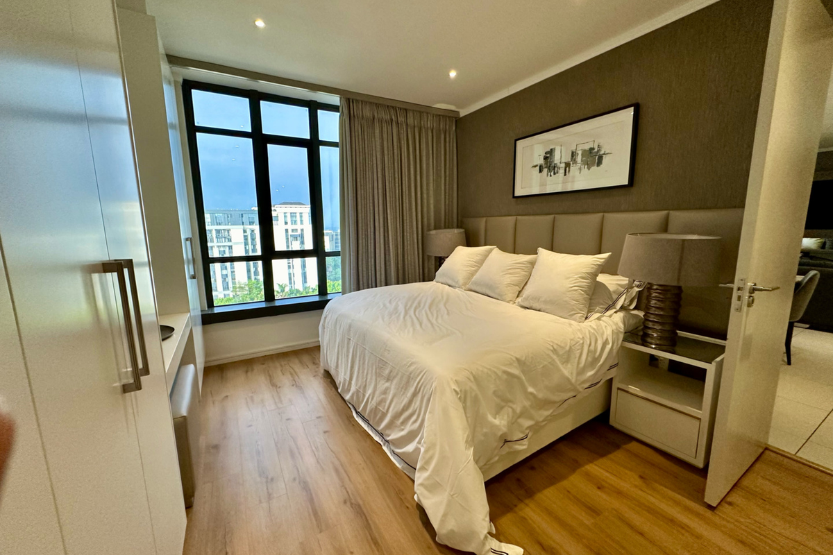A well-maintained bedroom featuring wood-look flooring, a large window with city views, recessed ceiling lighting, and a built-in wardrobe.