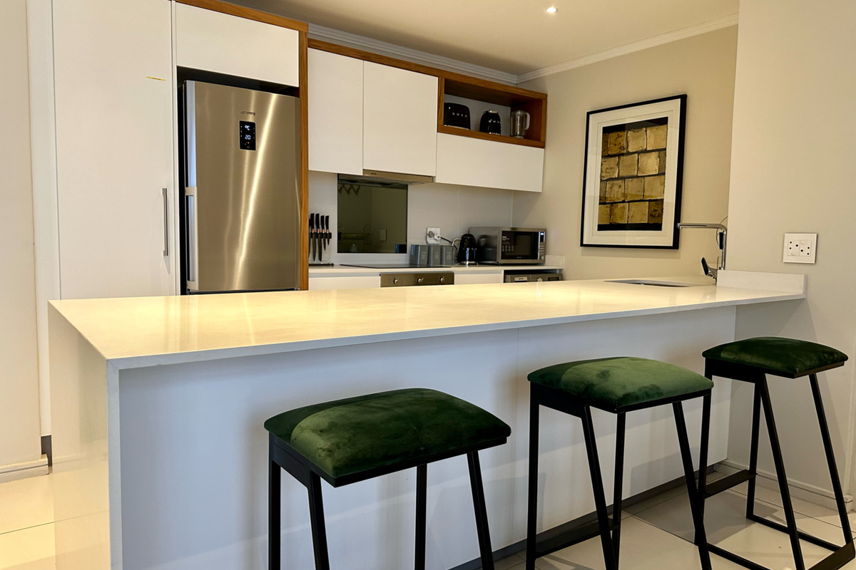 Modern kitchen featuring a sleek white breakfast bar, integrated cabinetry, and stainless steel appliances, offering a clean and functional culinary space.