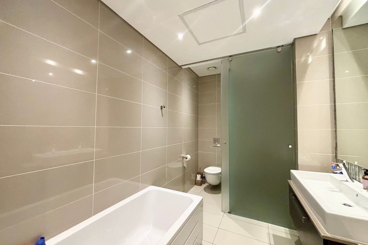 Modern bathroom featuring a built-in bathtub, wall-mounted toilet, vanity basin, and a frosted glass sliding door for privacy.