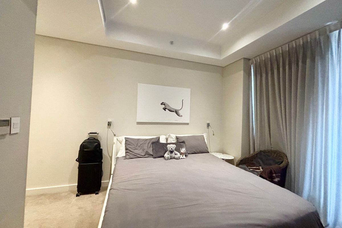 A well-maintained bedroom featuring a recessed ceiling with integrated downlighting and floor-to-ceiling curtains.