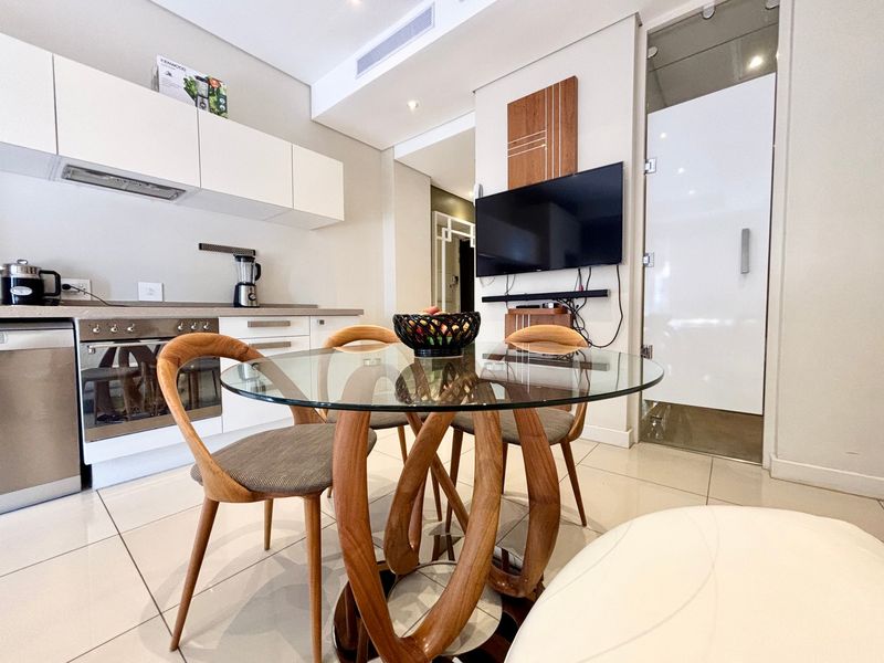Modern open-plan living and kitchen area featuring sleek white cabinetry, integrated appliances, tiled flooring, and contemporary finishes in a well-maintained apartment setting.