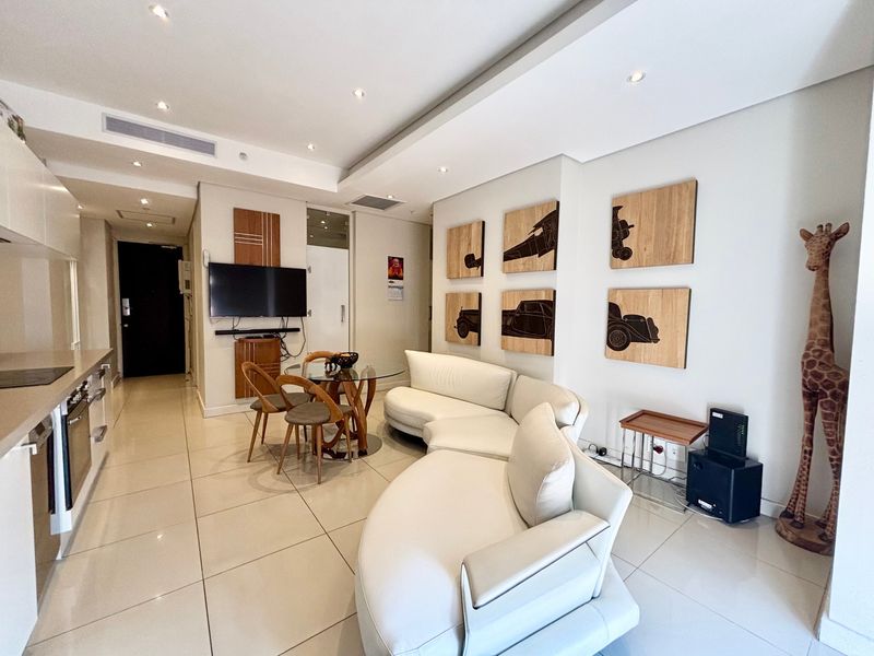 Modern open-plan living area featuring sleek porcelain floor tiles, recessed downlighting, and a compact integrated kitchen with built-in appliances.