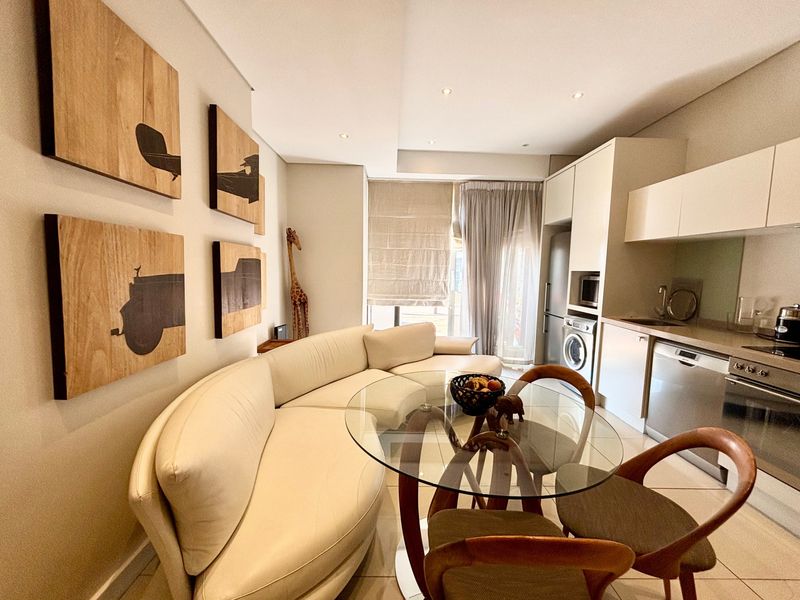 Modern open-plan living and kitchen area featuring sleek built-in cabinetry, integrated appliances, recessed lighting, and neutral tiled flooring.