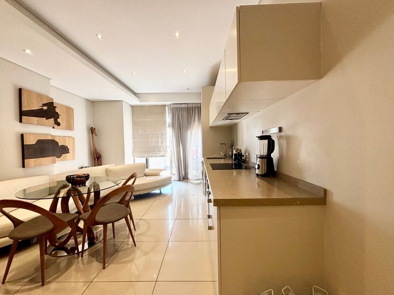 Modern open-plan living area featuring a sleek kitchen with stone countertops, integrated hob, and recessed lighting, seamlessly flowing into the dining and lounge space.
