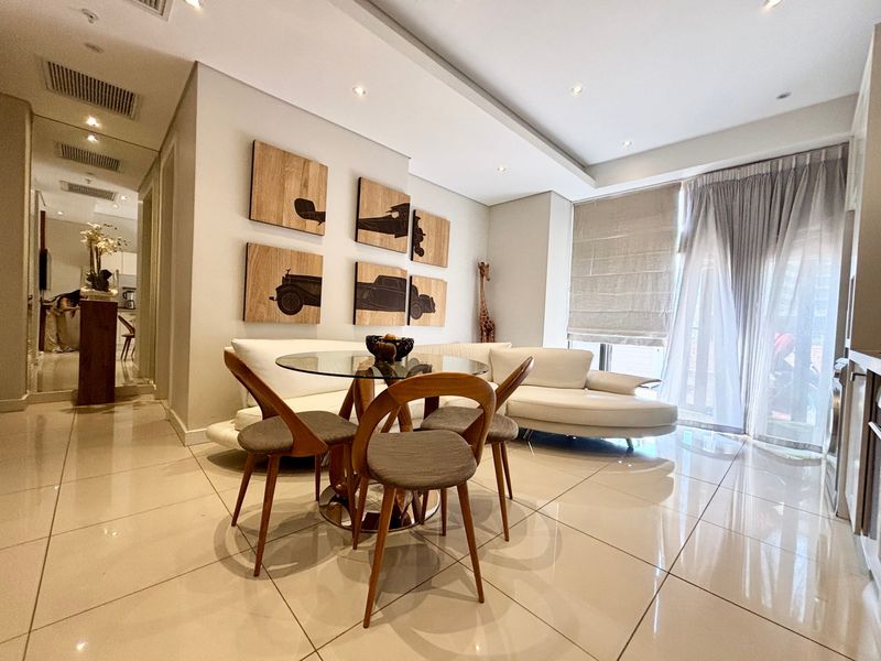 Modern open-plan living and dining area featuring polished tiled flooring, recessed ceiling lighting, and a mirrored wall accent.
