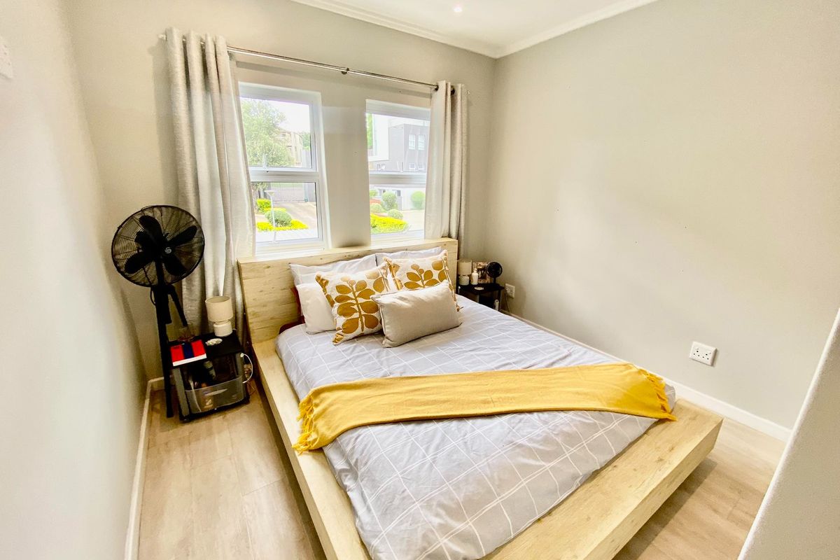 A well-maintained bedroom featuring light wood-look flooring, neutral wall tones, and double windows that provide natural light.