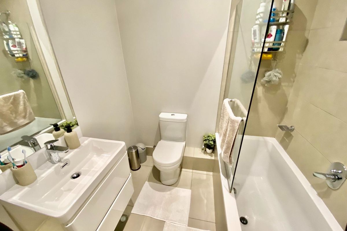 A compact, modern bathroom featuring a white vanity with integrated basin, a toilet, and a shower-over-bath combination with a glass screen.