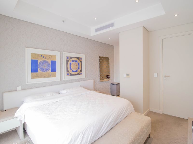 A well-maintained bedroom featuring neutral textured wallpaper, recessed ceiling lighting, and integrated ducted air conditioning.