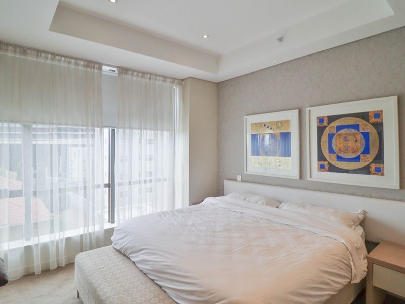A well-maintained bedroom featuring a recessed ceiling with downlights, textured wallpaper, and a large window providing natural light.
