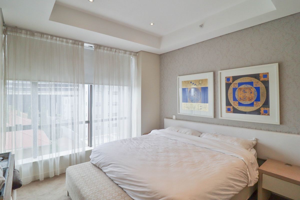 A well-maintained bedroom featuring a recessed ceiling with downlights, textured wallpaper, and a large window providing natural light.