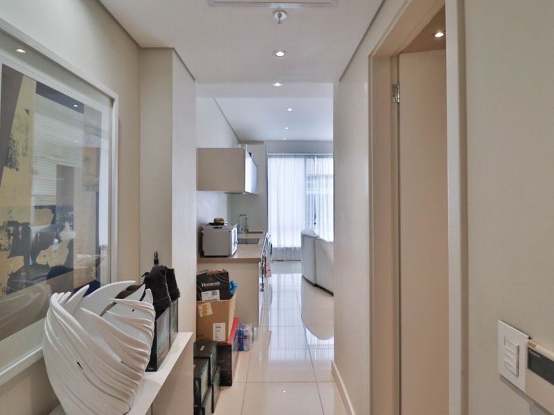 A bright hallway with polished tile flooring and recessed lighting, leading directly into an open-plan kitchen and living area.