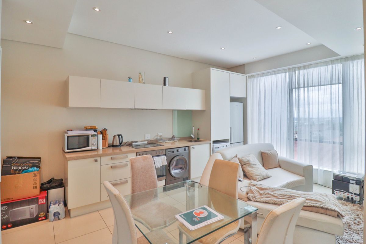 Modern open-plan apartment living area featuring a compact kitchen with built-in cabinetry, integrated appliances, and tiled flooring, leading to a bright living space.