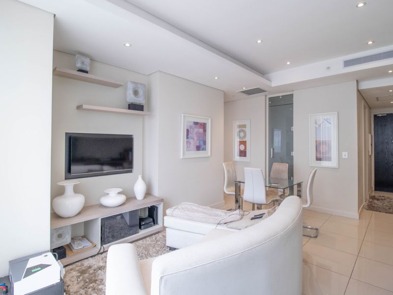 Modern open-plan living and dining area featuring neutral tones, recessed ceiling lighting, ducted air conditioning, and sleek tiled flooring throughout.