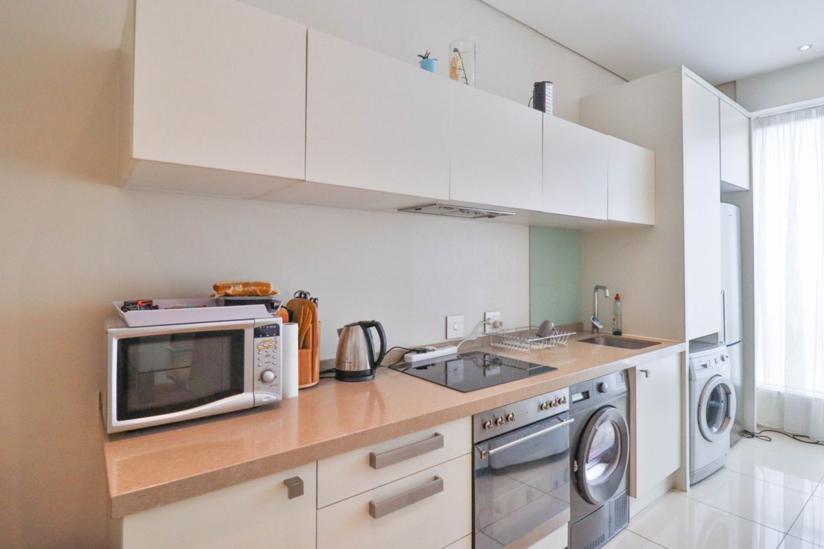 Modern kitchen featuring sleek white cabinetry, stone countertops, integrated appliances including an oven, hob, and washing machine, with clean finishes throughout.