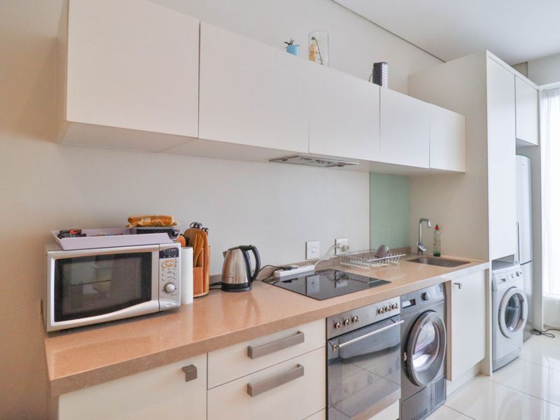 Modern kitchen featuring sleek white cabinetry, stone countertops, integrated appliances including an oven, hob, and washing machine, with clean finishes throughout.