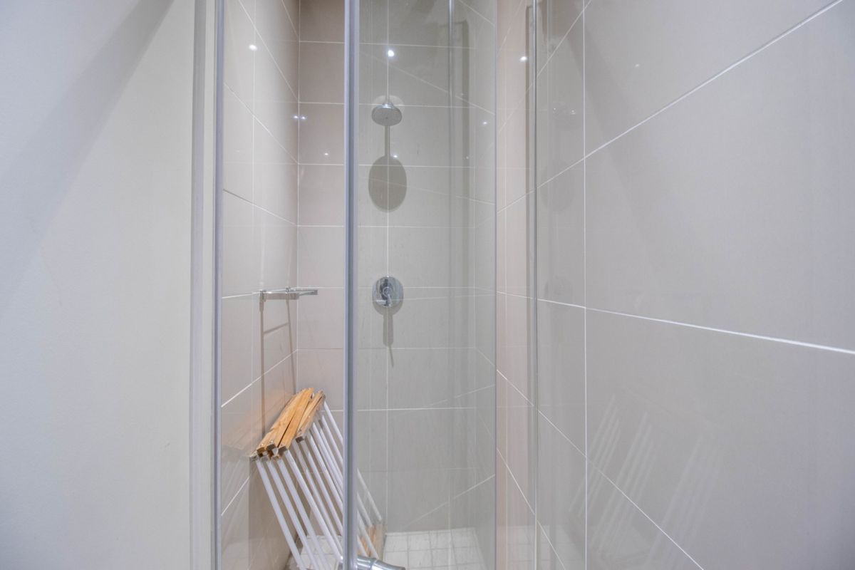 A modern, clean bathroom shower enclosure featuring neutral wall tiling, a fixed shower head, and integrated mixer tap.