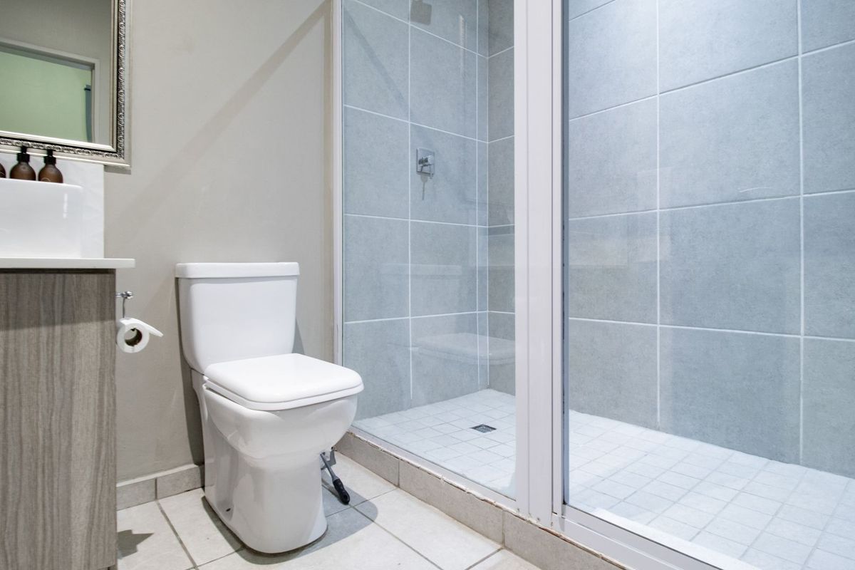 Modern bathroom featuring a vanity with basin, a white toilet, and a glass-enclosed shower with light grey wall tiles.
