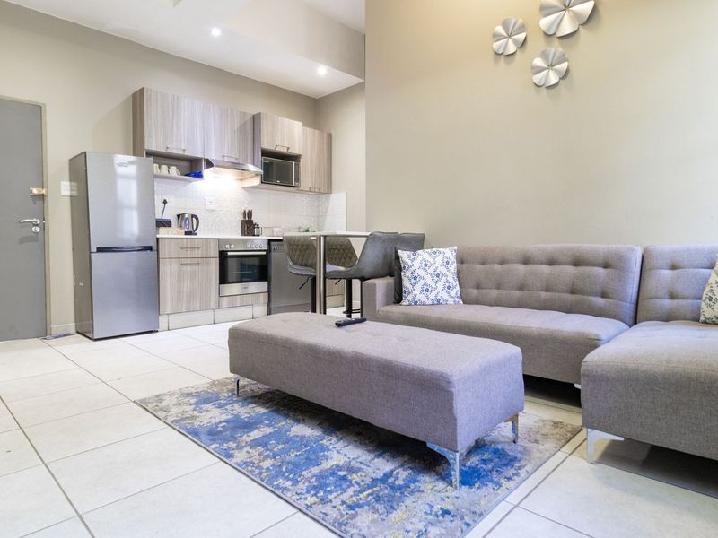 Modern open-plan apartment featuring a compact kitchen with built-in cabinetry and appliances, seamlessly flowing into a comfortable living area with tiled flooring.